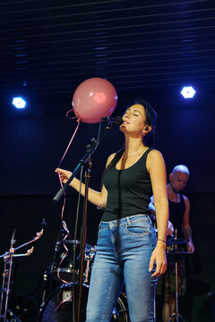Female singer performs sound check on dark concert stage with pink balloon