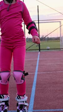 Little girl in pink outfit and protective gear roller skating outdoors on sports court at dusk