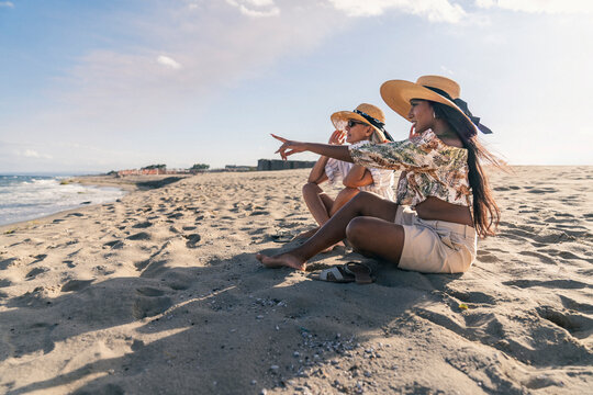 Young woman pointing toward the sea while sitting with a senior friend