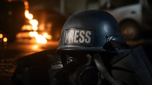 Press helmet and camera resting on ground near burning fire at night in conflict zone photojournalism
