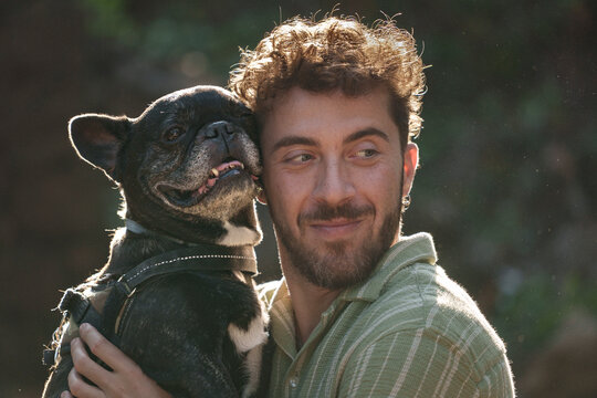 Young man cuddling his black French bulldog outdoors