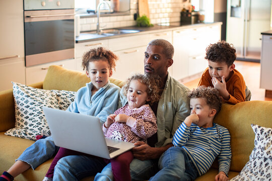 Man and four children watching laptop on sofa