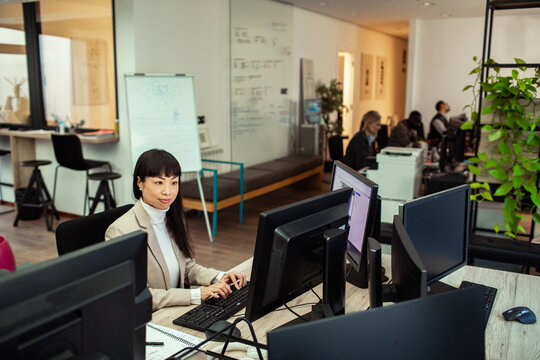 Woman typing at multi-monitor workstation in open office
