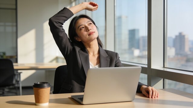 Professional young woman doing an arm stretch during a busy workday in the office