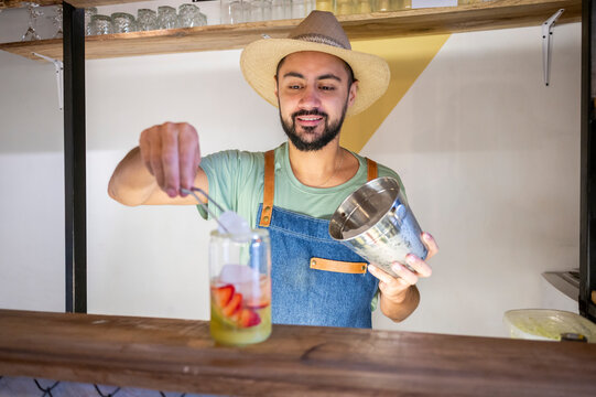 Bartender preparing a strawberry cocktail adding ice cubes to the glass