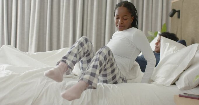 African American couple in bedroom, morning urging woman sitting in PJs reaching glass and drinking