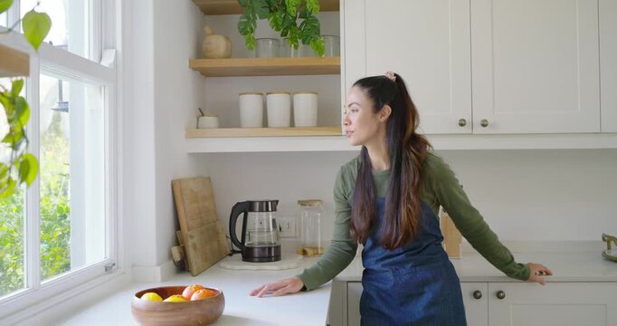 Asian woman smiling and laughing as camera pulling in at kitchen counter, engaging off-frame, apron