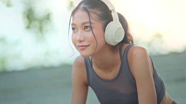 Close up of young Asian woman in sportswear using smartphone while taking a break from outdoor workout, female athlete wearing wireless headphones and smartwatch