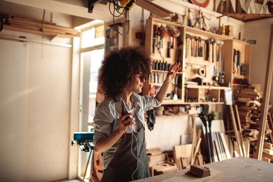Woman dancing with smartphone in woodworking workshop