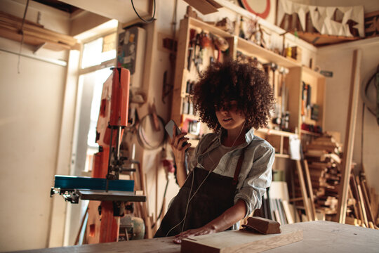 Woman woodworker checking smartphone in carpentry workshop