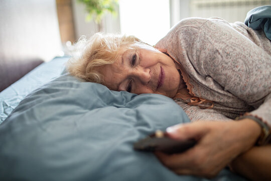 Senior woman relaxing in bed with remote control