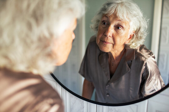 Senior woman inspecting her face in the bathroom mirror