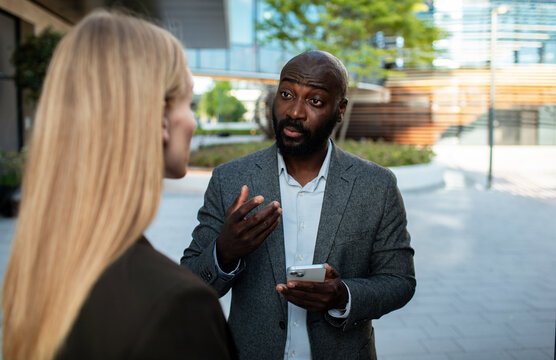 Businessman explaining to colleague outdoors with smartphone