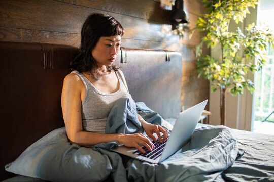 Woman typing on laptop in bed at home