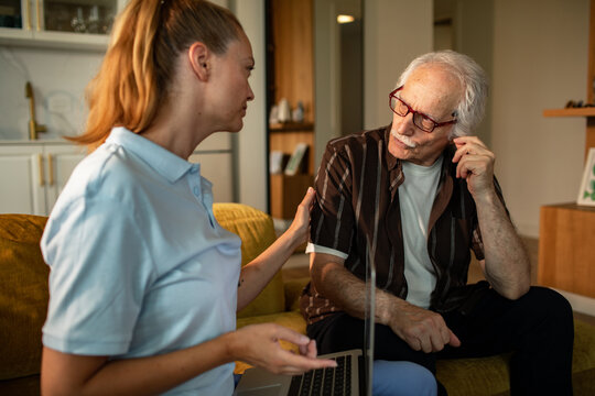 Caregiver discussing information on laptop with senior man at home