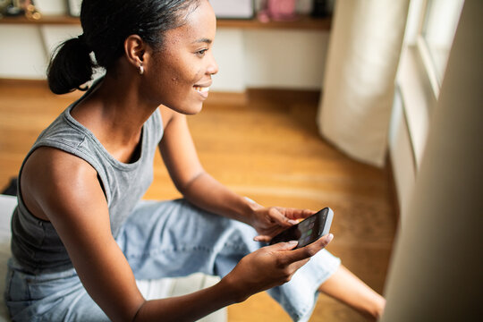 Smiling woman using smartphone by window at home