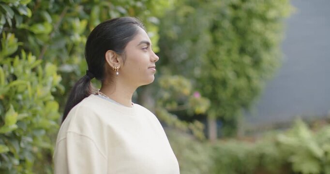 Adult woman turning from strict profile to smiling in front of hedge while camera framing widening