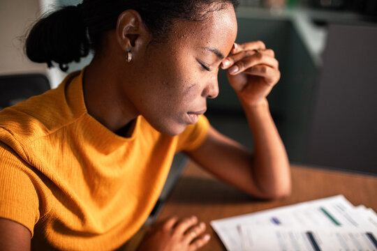 Stressed woman holding forehead over bills at desk