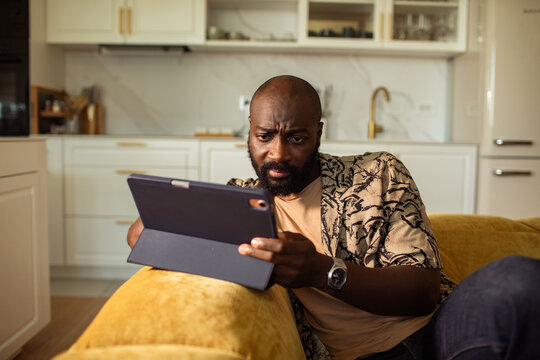 Man frowning at tablet on sofa at home