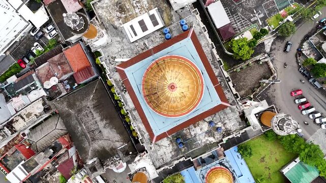 Aerial view of the golden dome of Masjid Agung Kota Sukabumi surrounded by urban rooftops and parking area in Sukabumi, West Java, Indonesia.