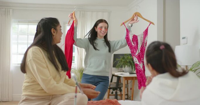 Diverse women friends seeing woman entering holding dresses on hangers at home modeling for input