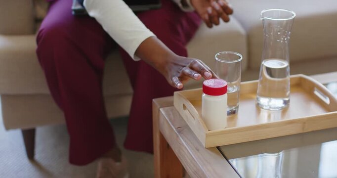 Grasping pill bottle on coffee table, woman in scrubs is dispensing pills into palm for dose