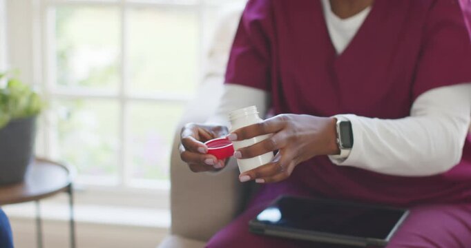 Nurse checking tablet, pouring from white bottle into cap, tipping into male patient's palm at home