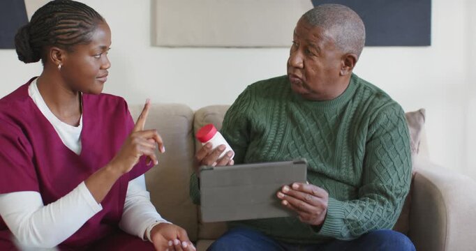African American nurse in scrubs explaining meds steps on tablet while man holding bottle at home