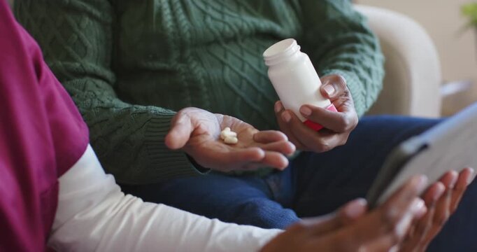Caregiver pouring capsules into patient palm while patient checking tablet for dosage at home