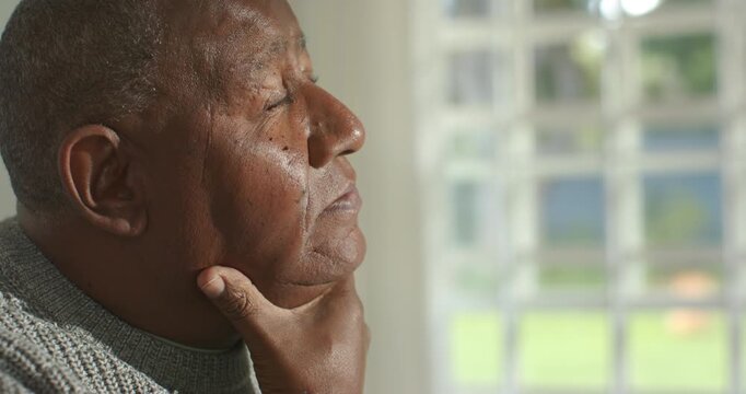 Senior African man home reacting to light pressing cheek cupping chin gazing out window reflecting