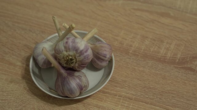 Fresh garlic bulbs and separated cloves arranged on a small plate, representing natural cooking ingredients, healthy food preparation and traditional home cuisine