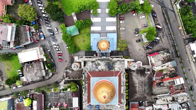 Aerial view of Masjid Agung Kota Sukabumi with its golden dome and minarets surrounded by urban rooftops and streets in Sukabumi, West Java, Indonesia.