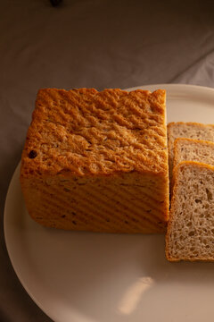 Top view of rectangular whole grain loaf and several sliced pieces arranged on white plate, showing crust texture and interior crumb details.