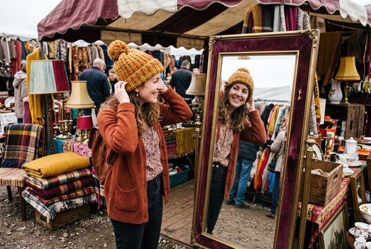 Vintage market shopper tries on hat beside mirror