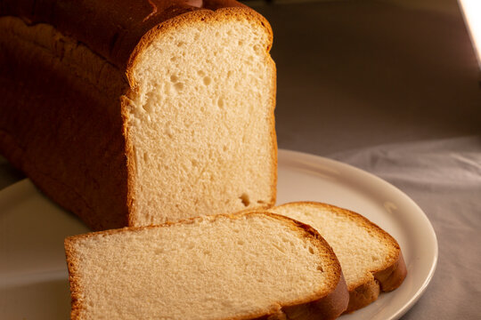 Close-up view of several slices cut from white bread loaf arranged on white plate with crust and soft crumb texture visible under warm lighting.