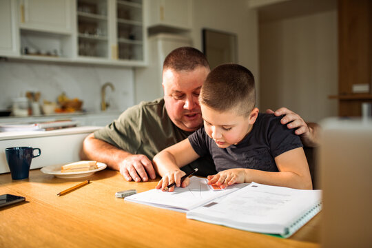 Father helping son with math homework at kitchen table