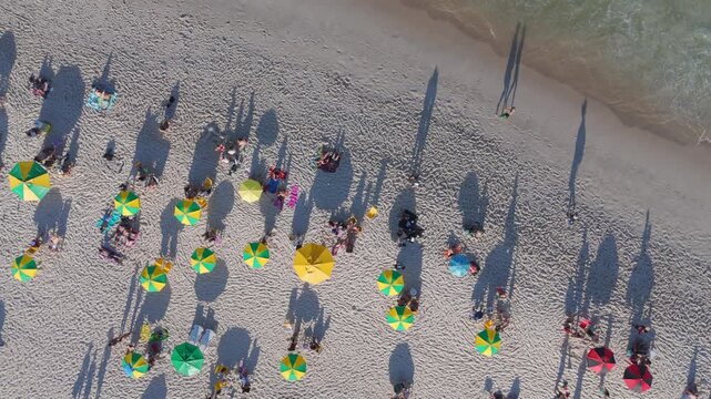 Top-down aerial view of colorful umbrellas and beachgoers on Copacabana Beach as waves roll onto the sand, Rio de Janeiro, Brazil.