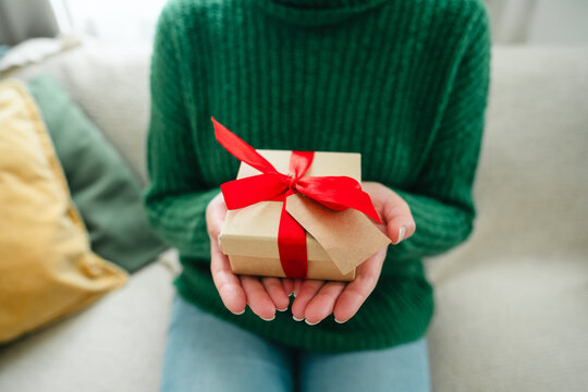 Woman holding a wrapped Christmas gift with a red ribbon at home