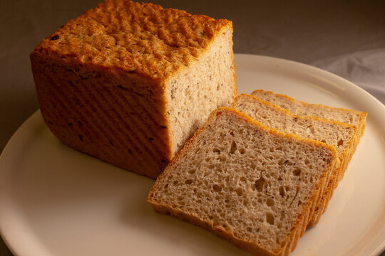 Close view of square multigrain loaf with three bread slices on white plate, highlighting toasted crust texture, visible grains, and soft crumb.