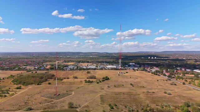 Aerial view of the Lakihegy radio mast over dry grassland, industrial buildings and residential areas in Szigetszentmikl&oacute;s, Hungary, beneath scattered clouds.