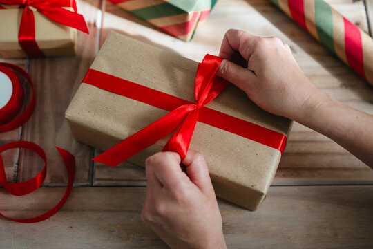 Close up of hands tying a ribbon around a wrapped Christmas gift