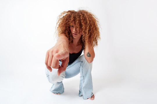 Hispanic woman with curly red hair crouching and pointing