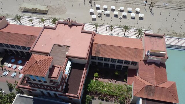 Top down drone flight over a sandy beach, turquoise sea and red tiled resort roofs in Tarragona, Spain