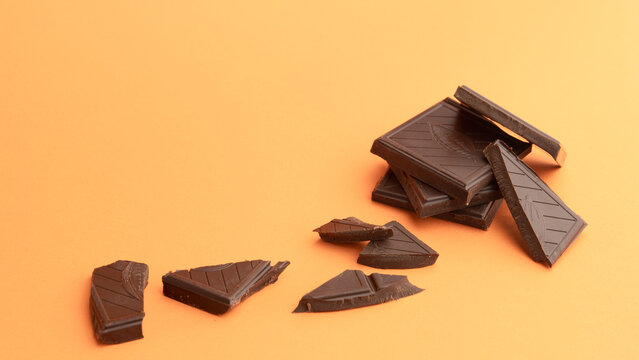 Trozos de chocolate negro gourmet y ramas de canela sobre un fondo naranja minimalista con espacio para texto
