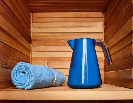 wooden sauna interior with loofahs and blue water jug on wooden shelf