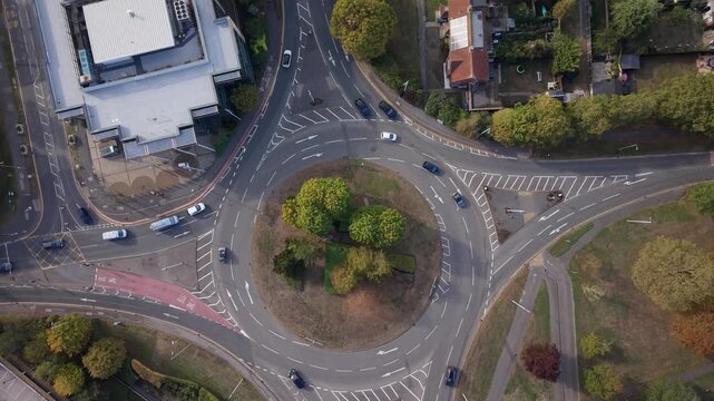 Top view traffic roundabout: Aerial drone footage of a busy road intersection, driving cars, a multi-lane circle, urban transport network, parking lots, and daytime city infrastructure video under bri