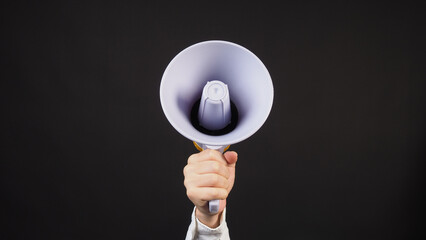 Fototapeta premium Hand holding a white megaphone against a dark background