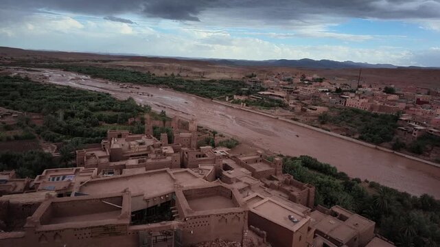 Aerial drone view capturing the historic earthen clay architecture and mud-brick houses of the UNESCO ksar of A&iuml;t Benhaddou along the river in Morocco
