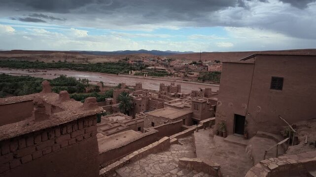 Elevated high-angle pan overlooking the historic mud-brick rooftops and winding pathways of the ancient fortified ksar at A&iuml;t Benhaddou in Morocco.