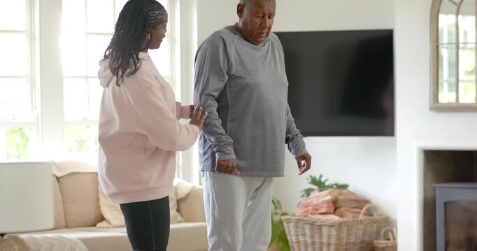 Female caregiver prompted by dumbbells guiding mature man adjusting posture and arm in living room